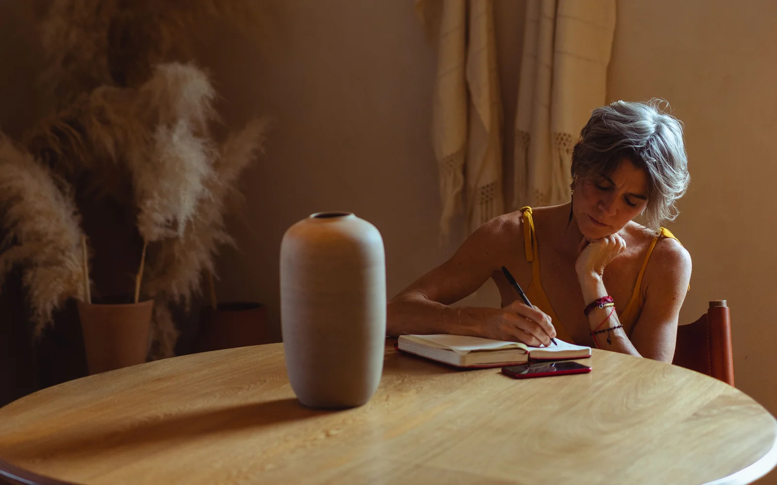 Vrouw met grijs haar schrijft aan een ronde houten tafel in een schrift