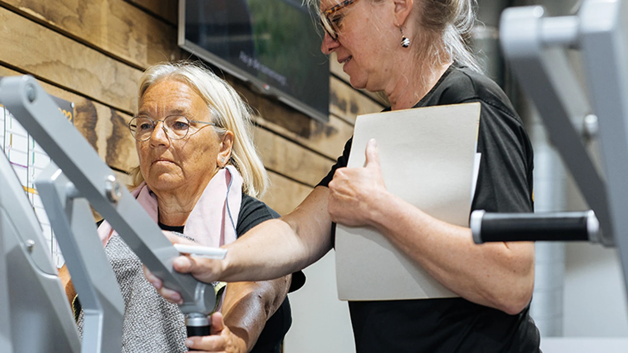 Coach begeleidt een oudere vrouw aan een krachttoestel